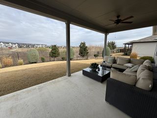 Model Home A cozy patio with a comfortable sectional sofa, coffee table, and fan overlooking a landscaped yard with a scenic view.
