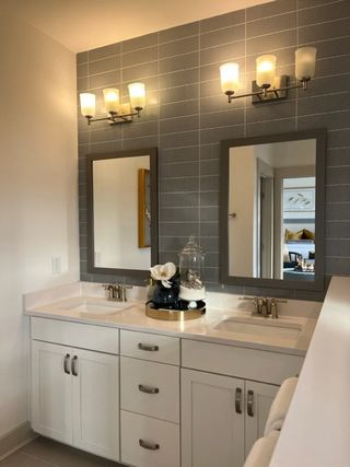 A chic bathroom featuring a dual-sink vanity, grey tile wall, and modern lighting fixtures.