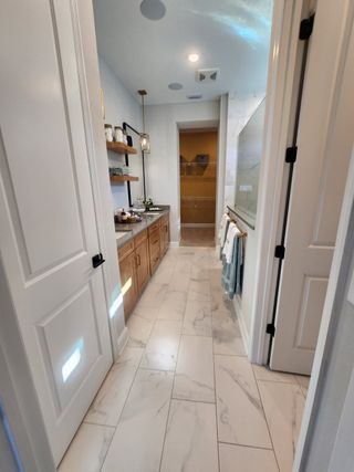 A luxurious bathroom featuring marble-style flooring, wooden cabinetry, and elegant lighting, leading to a spacious walk-in closet.