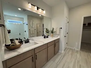 A close-up of the double vanity with beautiful wooden cabinetry, black fixtures, and a wide mirror reflecting soft, neutral decor.