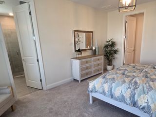 A serene primary bedroom with soft neutral tones, cozy carpet, and modern lighting offers a tranquil escape.