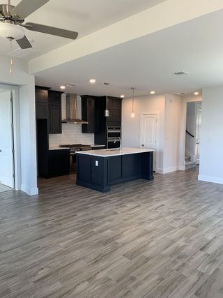Model Home An open kitchen with dark cabinetry, white island, stainless steel appliances, and wood-style flooring. Modern and inviting.