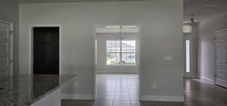 A bright interior with a granite countertop, a tiled floor, and natural light streaming through large windows and a sleek chandelier.