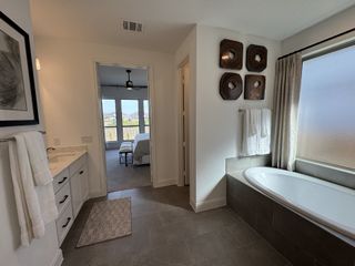A modern bathroom featuring a sleek bathtub, elegant vanity, and stylish wall art, with a view into the bright bedroom beyond.