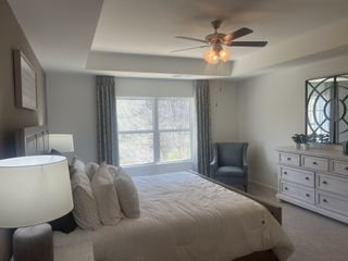 Model Home A cozy bedroom with a tray ceiling, soft lighting, elegant curtains, and a stylish mirror above a dresser.