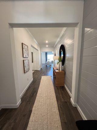 A modern hallway with dark wood flooring, white walls, and stylish decor leading to a bright living area.