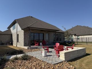 A backyard patio with red Adirondack chairs, stone firepit, and lush landscaping in Blackhawk by GFO Home (Pflugerville, TX).