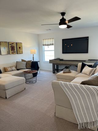 A cozy living room with beige seating, modern fan, game table, and playful wall art. Perfect for relaxing and entertaining.