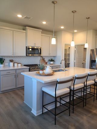 Model Home A modern kitchen with white cabinets, a spacious island with seating, and elegant pendant lighting.