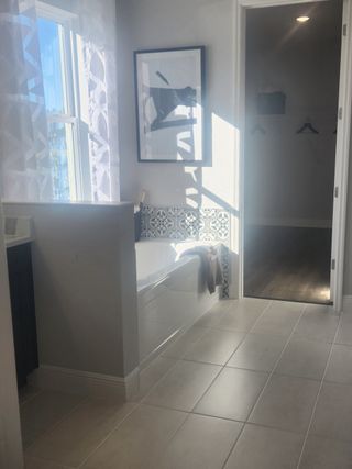 A sunlit bathroom featuring a sleek bathtub, patterned tiles, and elegant wall art for a modern touch.