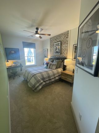 A cozy bedroom featuring plaid bedding, a brick accent wall, and a modern workspace, creating an inviting retreat.