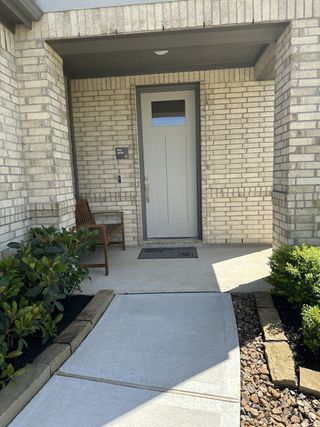 A welcoming entry with light brick, manicured shrubs, and a cozy bench in Bauer Meadow by KB Home (Hockley, TX).
