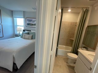 Model Home A cozy bedroom with soft lighting leads into a compact bathroom featuring a tiled bathtub and a sleek vanity.