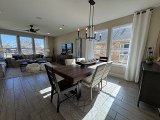 Model Home A bright living and dining area with large windows, wood floors, modern chandelier, and cozy seating for entertaining.