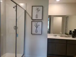 Model Home A modern bathroom features a glass shower, elegant vanity, and tasteful framed botanical artwork.