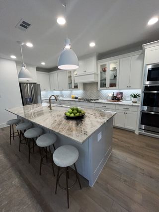 A bright, modern kitchen features white shaker cabinets, a large quartz island with seating, and stainless steel appliances, creating a perfect space for culinary enthusiasts.