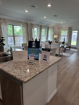 A bright living space with a granite kitchen island, wood floors, and large windows letting in natural light.