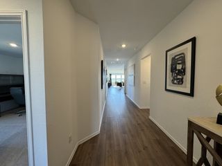A modern hallway with wooden floors, white walls, and contemporary artwork, leading to a bright, airy living space.