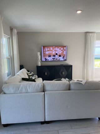A cozy living room with a plush white sectional sofa, modern TV stand, and soft natural light filtering through sheer curtains.