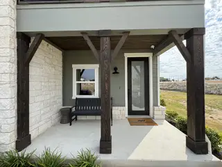 Charming porch with rustic wooden beams and stone accents in Covered Bridge by Ashton Woods (Hutto, TX).
