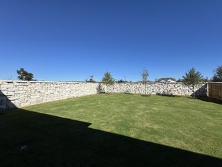 A spacious backyard with stone walls and a manicured lawn in 6 Creeks by New Home Co. (Kyle, TX).