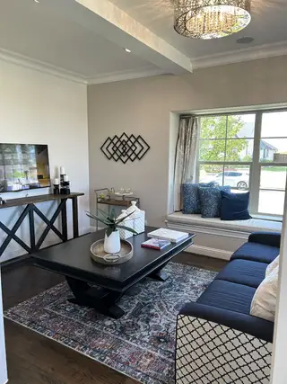 A cozy living room with a patterned rug, chic chandelier, navy seating, and a charming window nook.