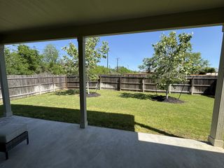 Model Home A spacious backyard with a covered patio, green lawn, and young trees enclosed by a wooden fence.