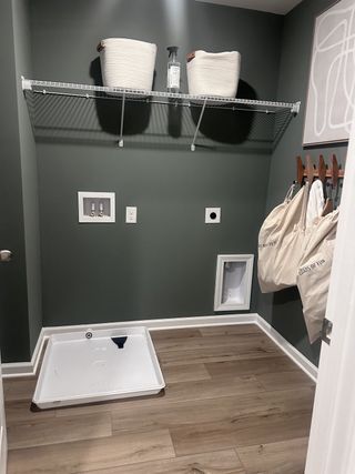 A sleek laundry room featuring green walls, wood flooring, utility hookups, and organized storage baskets.