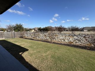 A spacious backyard with a stone wall and wooden fence in Oaks at San Gabriel by Brightland Homes (Georgetown, TX).