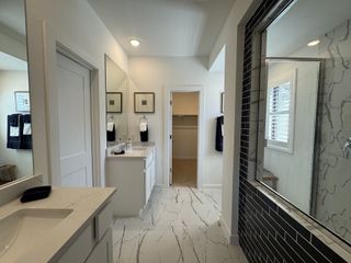 A modern bathroom featuring dual sinks, elegant marble surfaces, and sleek black tile accents with ample natural light.