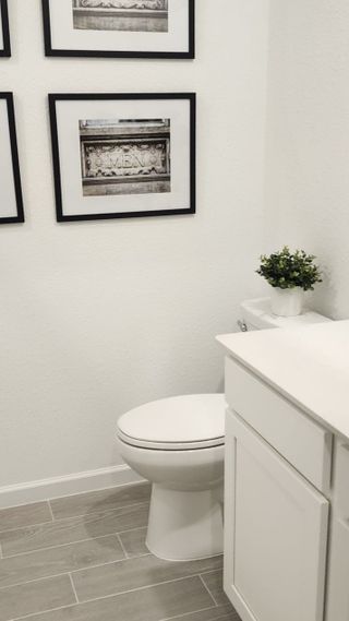 A bright powder room with a white vanity, framed wall art, and sleek tile flooring for a fresh and modern touch.