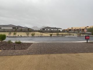A wide street with newly built homes in neutral tones, desert landscaping, and mountain views under a cloudy sky in Aloravita South by Taylor Morrison (Peoria, AZ).