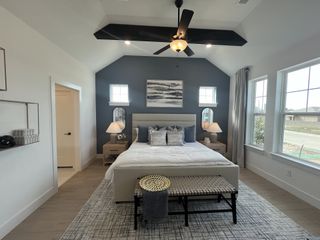Model Home A cozy bedroom featuring a vaulted ceiling, dark accent wall, modern ceiling fan, and ample natural light.