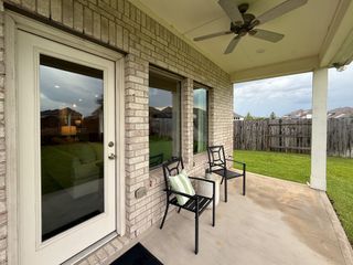 A cozy patio with seating, brick exterior, and ceiling fan overlooking a fenced green yard. Perfect for relaxing outdoors.