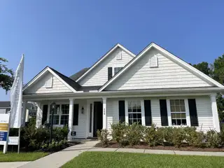 Street view A charming white home with black shutters and inviting porch in High Point at Foxbank by Dream Finders Homes (Moncks Corner, SC).