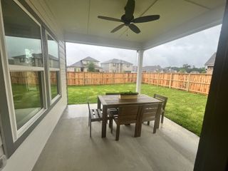 A cozy covered patio with a ceiling fan, outdoor furniture, and a view of a fenced backyard, perfect for relaxation.
