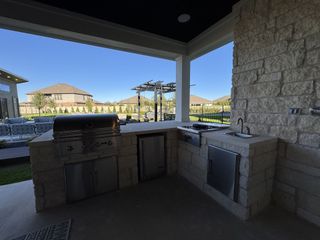 A covered outdoor kitchen with a stone countertop, built-in grill, and sink overlooking a landscaped backyard with seating.