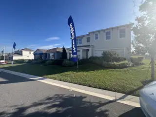 A beautiful model home with lush landscaping and blue "Now Selling" banners in Cypress Park Estates by D.R. Horton (Haines City, FL).