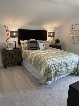 A cozy bedroom featuring a striped bedspread, stylish lamps, and baseball-themed decor on a sloped ceiling.
