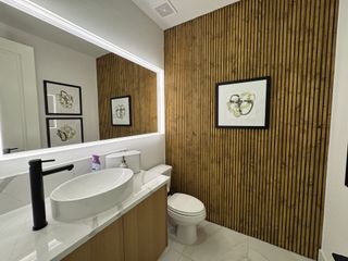 A modern bathroom featuring a vessel sink, sleek black faucet, wood accent wall, and contemporary artwork.