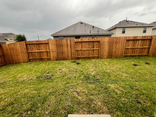 A private backyard with a tall wooden fence, lush green grass, and plenty of space for outdoor activities.