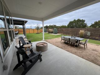 A covered patio with cozy seating, fire pit, and dining area overlooking a landscaped backyard.