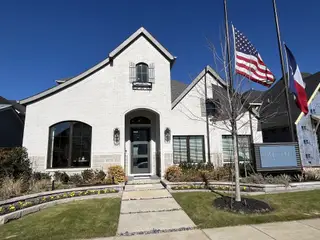 A striking white brick home with elegant shutters and lush landscaping in The Tribute by Britton Homes (Frisco, TX).