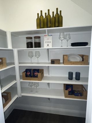 Model Home A neatly organized pantry with white shelves, wine bottles, and kitchenware, offering ample storage space.