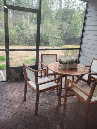 Model Home A cozy screened patio with brick flooring, featuring a round wooden table and chairs, overlooking a lush green backyard.