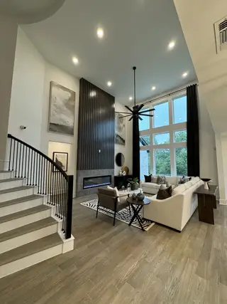 A modern living room with high ceilings, large windows, a sleek fireplace, and elegant decor in neutral tones.