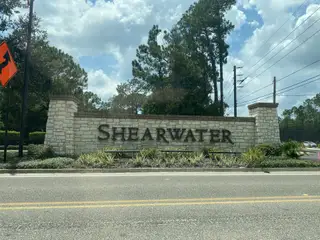 A welcoming stone entrance sign in Shearwater: Shearwater - Single Family by Lennar in St. Augustine, FL, enhanced with greenery.
