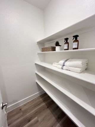 Model Home A neatly organized storage space with white built-in shelves, decorative accents, and towels on light-colored flooring.