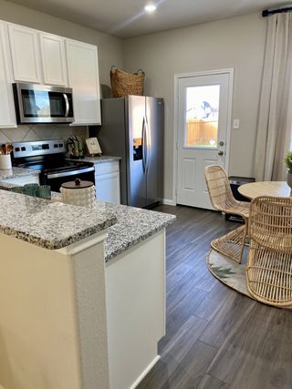 Model Home A modern kitchen with white cabinets, granite countertops, stainless appliances, and a cozy dining area with wicker chairs.