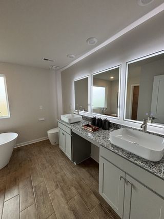 Contemporary bathroom featuring dual vanities, granite counters, wood-look tile, and a freestanding tub.